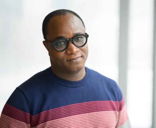 A middle aged black man with black framed glasses and a stripped red and blue sweater