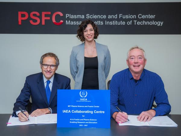 Three people smiling and facing a camera as they sign documents