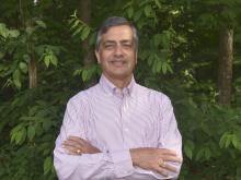 Abhay Ram standing with arms crossed in front of greenery.