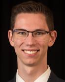 Headshot of Matthew Cufari; a young white man wearing a black jacket and white collared shirt. He has glasses and is smiling head on at the camera.