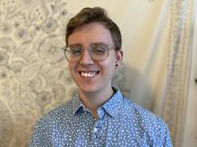 Conor Perks in blue shirt, smiling, with cream-colored background